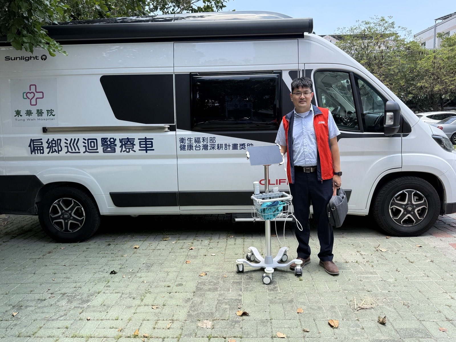 吳俊諺醫師站在東華醫院偏鄉巡迴醫療車前，一旁備有遠距醫療設備